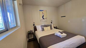 Een hotelkamer met een bed, nachtkastje, raam en een bord aan de muur.