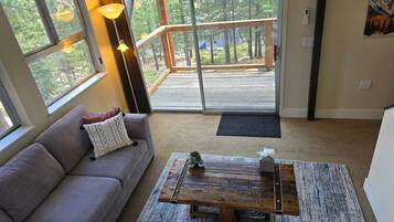 A living room with a sofa, a coffee table, and a view through a sliding glass door to an outdoor deck.