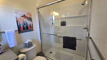 A bathroom with a glass-enclosed shower, a toilet, and a sink.