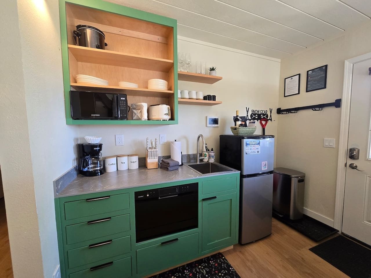 Een kleine keuken met groene kastjes, een vaatwasser, een koelkast en een koffiezetapparaat.