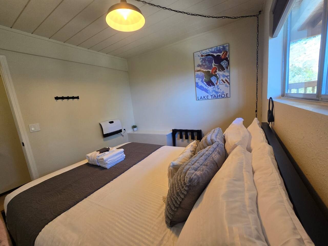 A hotel room with a bed, a poster on the wall, a window, and a bedside table.