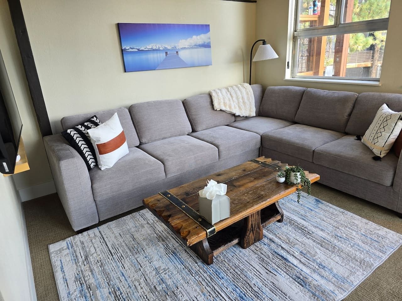 A living room with a grey sofa, a wooden coffee table, and a painting of a landscape on the wall.