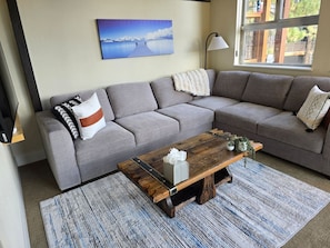 Un salon avec un canapé gris, une table basse en bois et un tableau représentant un paysage accroché au mur.
