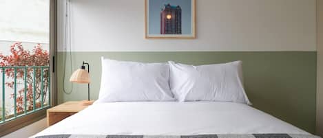 Habitación de hotel con una cama, una mesita de noche, una lámpara, un cuadro en la pared y vistas al exterior.