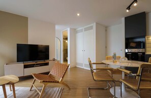 A modern living room with a flat-screen TV, a seating area with a sofa and chairs, a dining table with chairs, and a kitchen area with a microwave and stove. - w* | Amazing 2BR with Balcony in Prime Miraflores (Miraflores)