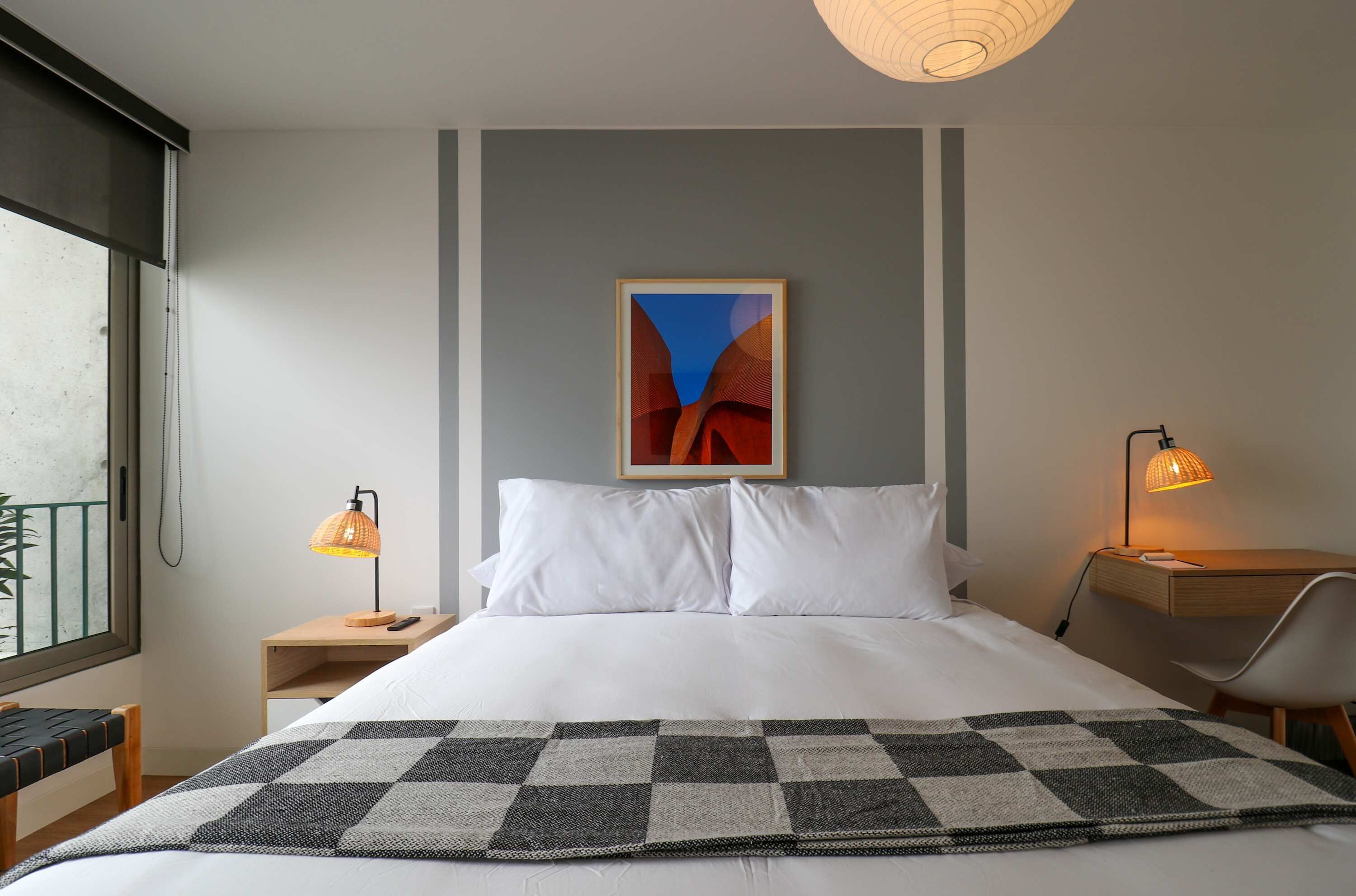A hotel room with a bed, a checkered throw, a painting on the wall, and two bedside lamps.