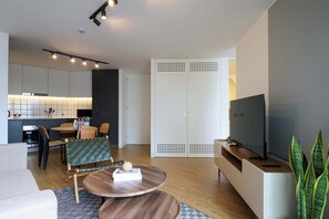 A modern living room with a sofa, a coffee table, a TV, and a kitchen area in the background. - w* | Upscale 2BR with Balcony in Prime Miraflores (Miraflores)