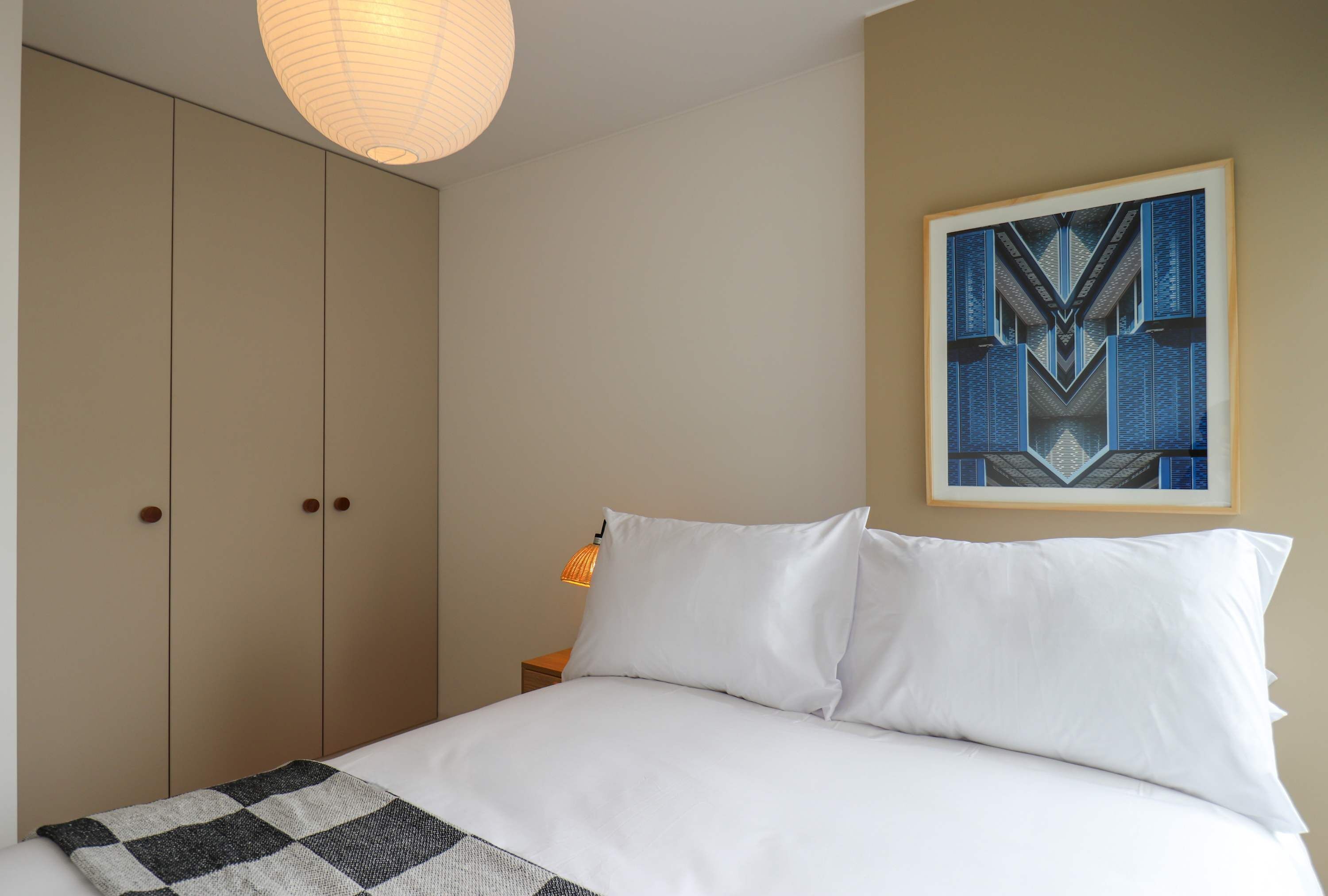A bedroom with a bed, a hanging light fixture, a framed abstract painting, and a wardrobe.