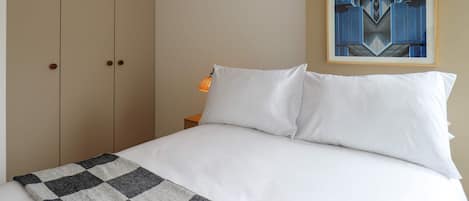 Un dormitorio con una cama, una lámpara colgante, un cuadro abstracto enmarcado y un armario.