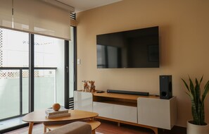 Un salon moderne avec un téléviseur à écran plat fixé au mur, une table basse en bois, un canapé et une plante en pot.