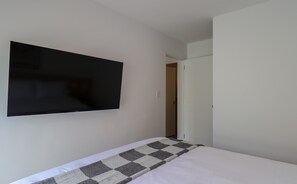 A room with a bed, a flat-screen TV mounted on the wall, and a door leading to another room. - w* | Enchanting 1BR w/ Balcony in Prime Miraflores (Miraflores)