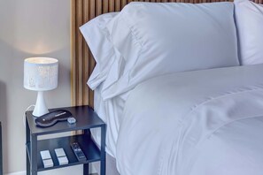 A neatly made bed with white linens, a bedside table with a lamp, and a remote control. - w* | Refined Loft w/ Balcony in Usaquen (Bogotá)