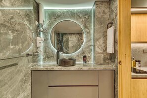 Een badkamer met een marmeren wastafelmeubel, een ronde spiegel, een handdoekhouder en een zeepdispenser.