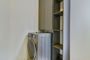 Uma lavanderia compacta com máquina de lavar de abertura frontal e secadora de metal, anexa a uma estante embutida.