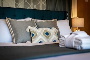 A neatly made bed with a blue headboard, two pillows, and a folded white towel on a hotel room.