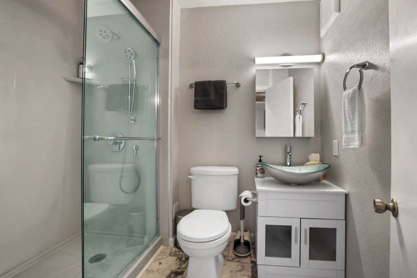Ein Badezimmer mit einer Duschkabine, einer weißen Toilette, einem Waschbecken mit Glasbecken und einem Spiegel über dem Waschbecken.