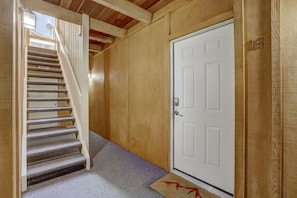 A wooden interior with a white door, a carpeted staircase, and a doormat.