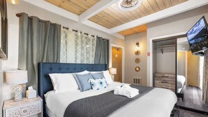 Ein Hotelzimmer mit einem großen Bett, einem Fernseher, einem Nachttisch mit Lampe und einem Kleiderschrank.