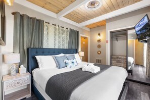 Et hotelværelse med en stor seng, et fjernsyn, et sengebord med lampe og et garderobeskab.