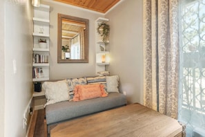 A cozy room with a sofa, a mirror, a bookshelf, and a window with curtains.