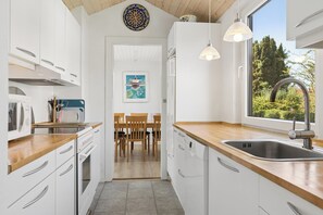 A modern kitchen with white cabinetry, a wooden countertop, a stainless steel sink, and a view of the outdoors. - Holiday home near central Gedser (Gedser)
