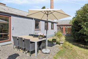 A patio with a table and chairs, a large umbrella, and a potted plant. - Holiday home near central Gedser (Gedser)
