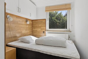 A bedroom with a bed, wooden headboard, two bedside lamps, a window with a view of trees, and a radiator. - Holiday home near central Gedser (Gedser)
