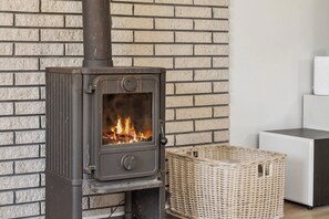 A wood-burning stove with a fire inside, set against a brick wall. - Holiday home near central Gedser (Gedser)