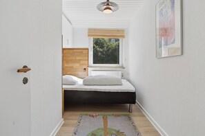 A narrow hallway leading to a bedroom with a bed, a window, and a radiator. - Holiday home near central Gedser (Gedser)