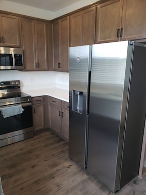 A kitchen with wooden cabinets, stainless steel appliances including a refrigerator, oven, and microwave, and a white countertop. - Charming bedroom in fantastic Spartanburg with cool AC (Spartanburg)