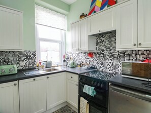 A kitchen with white cabinets, a black stove, and a window with blinds. - FLAT 3, family friendly, country holiday cottage in Llandudno (Llandudno)