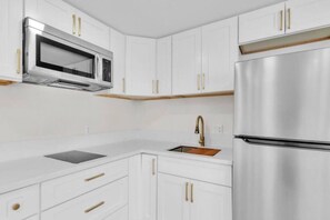 Eine moderne Küche mit weißen Schränken, einem Edelstahlkühlschrank, einer Mikrowelle und einem Waschbecken mit goldenem Wasserhahn.