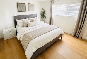 Ein Schlafzimmer mit einem Bett, Nachttischen, einer Pflanze und einem Fenster mit Vorhängen.