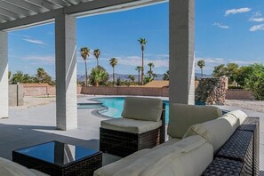 A covered outdoor area with a pool, lounge chairs, and a view of palm trees and mountains. - LUX 6BR 3 Suites 3 Kitchens Pool 2 Huge Backyard Firepit (Las Vegas)