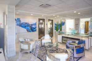 A modern lobby with a glass reception desk, white leather chairs, and abstract art on the walls. - Three Bedroom Beachfront | Top Floor | Panoramic Gulf Views | Heated Pool, Tiki Bar & Beach Access (Treasure Island)
