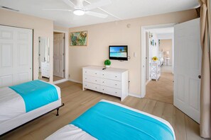 A hotel room with two beds, a TV, a ceiling fan, and a painting on the wall. - Three Bedroom Beachfront | Top Floor | Panoramic Gulf Views | Heated Pool, Tiki Bar & Beach Access (Treasure Island)