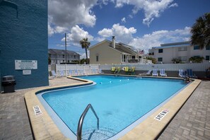 Una piscina con sillas de descanso, una torre de salvavidas y un cartel con las normas de la piscina.