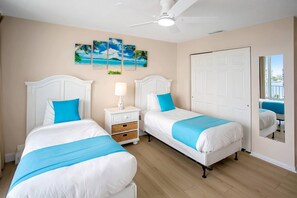 A hotel room with two beds, a ceiling fan, a door, and a window with a view. - Three Bedroom Beachfront | Top Floor | Panoramic Gulf Views | Heated Pool, Tiki Bar & Beach Access (Treasure Island)