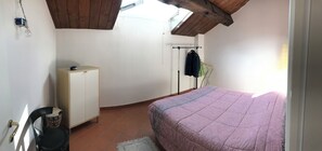 Ein Schlafzimmer mit Bett, Kleiderschrank, Heizkörper und Fenster.