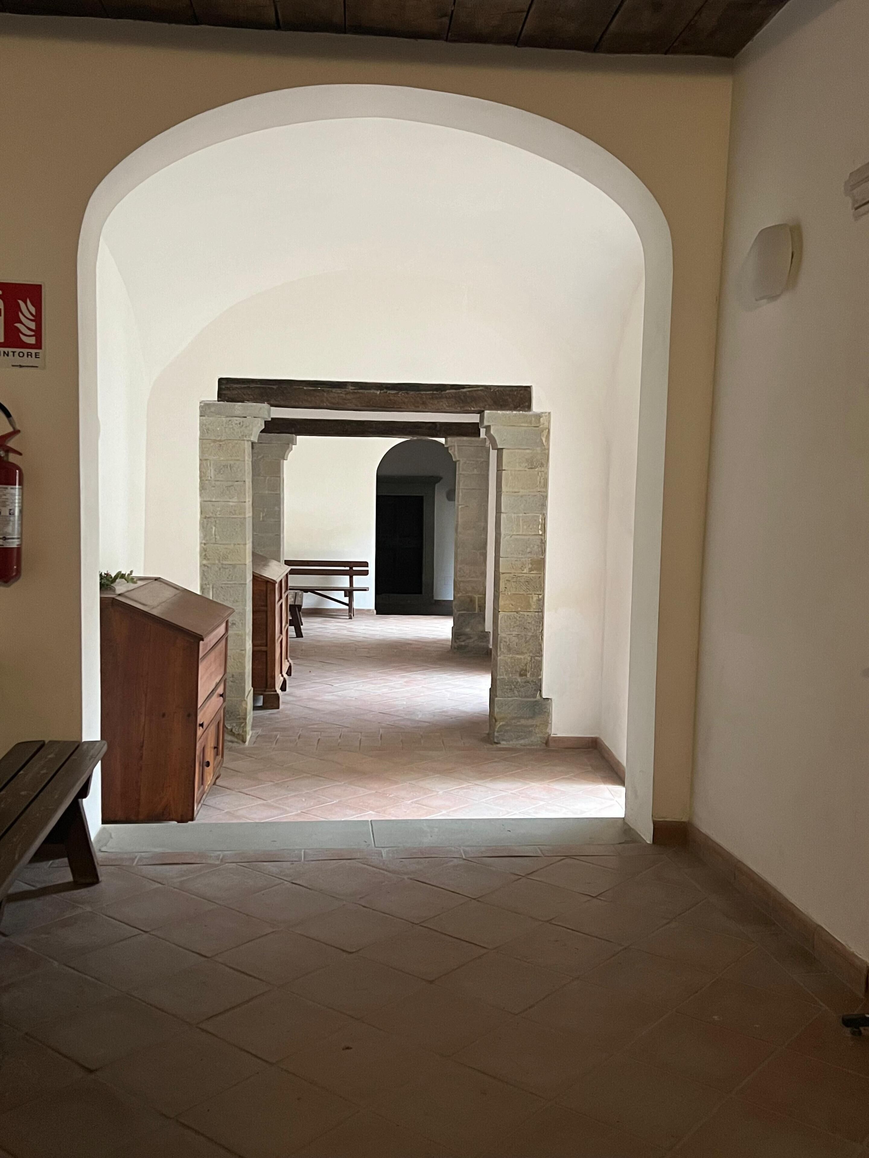 Um corredor com uma porta em arco que dá para um aposento com um banco e um armário de madeira.