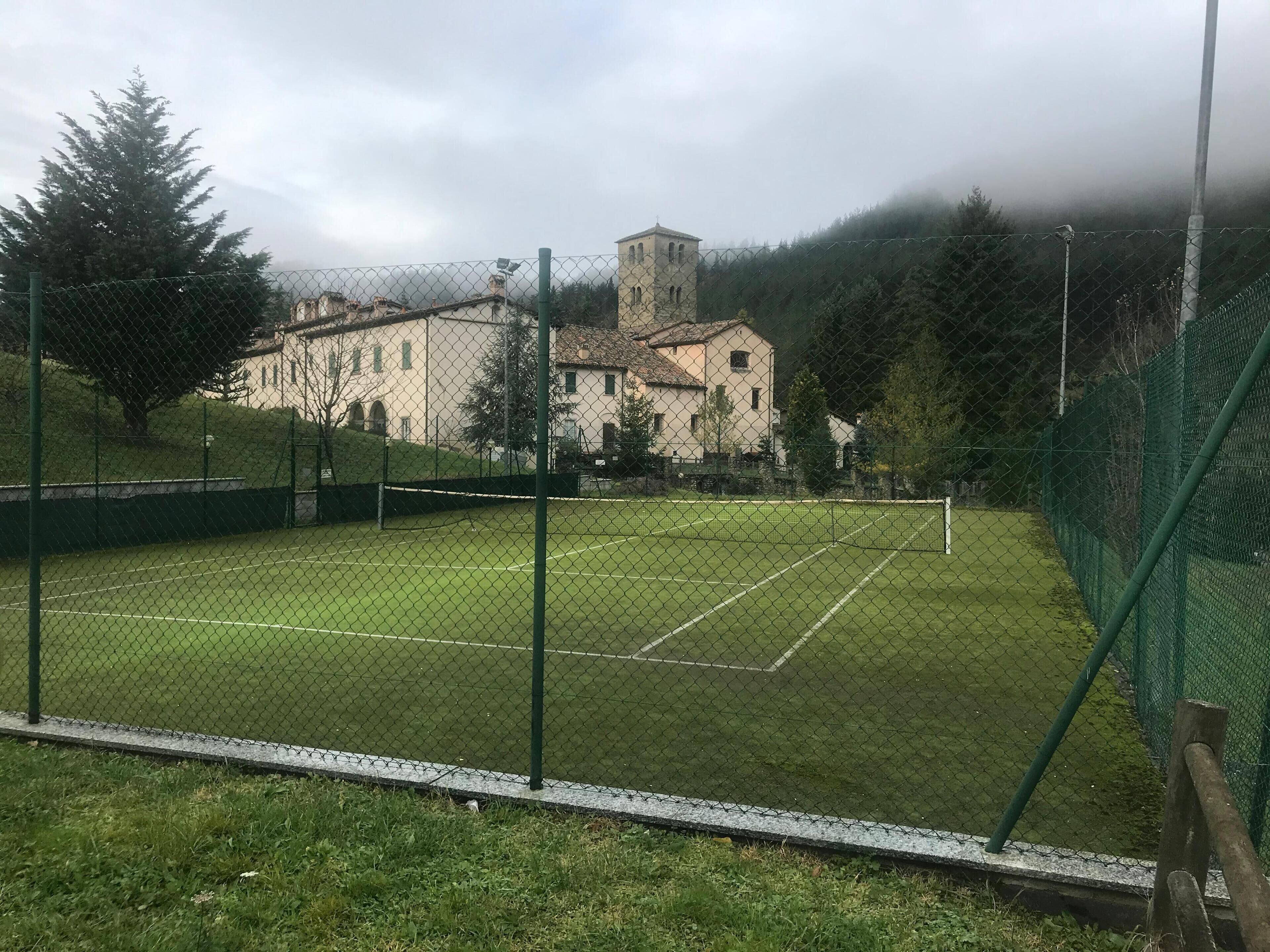 A tennis court surrounded by a chain-link fence with a building in the background.