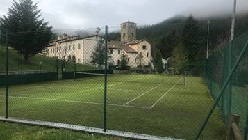 Ein Tennisplatz, umgeben von einem Maschendrahtzaun, mit einem Gebäude im Hintergrund.