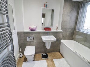 A modern bathroom with a white sink, toilet, and bathtub. There is a scale on the floor, a towel rack, and a mirror above the sink.
