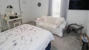 A bedroom with a bed, a desk, a chair, a television, and a window with curtains.