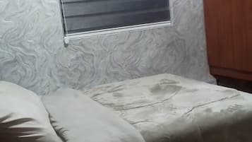 Une chambre avec un lit, une fenêtre avec des stores et une armoire en bois.