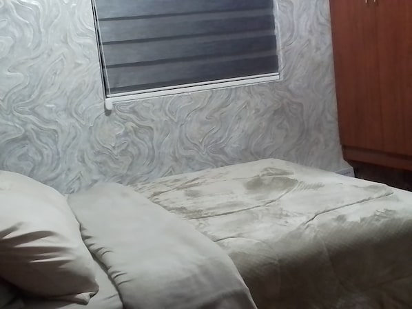A room with a bed, a window with blinds, and a wooden wardrobe.
