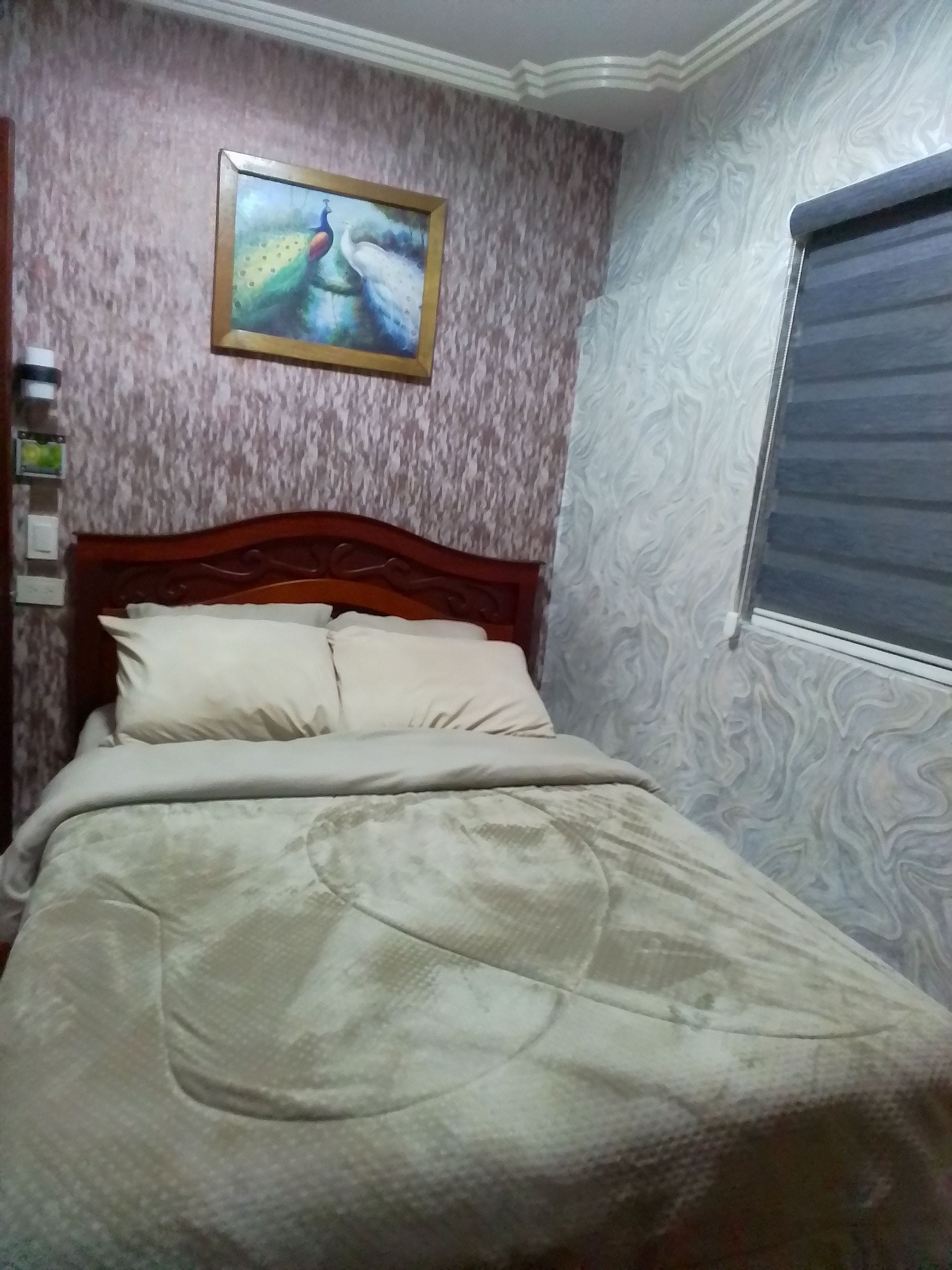 A bedroom with a bed, a painting on the wall, and a window with a blind.