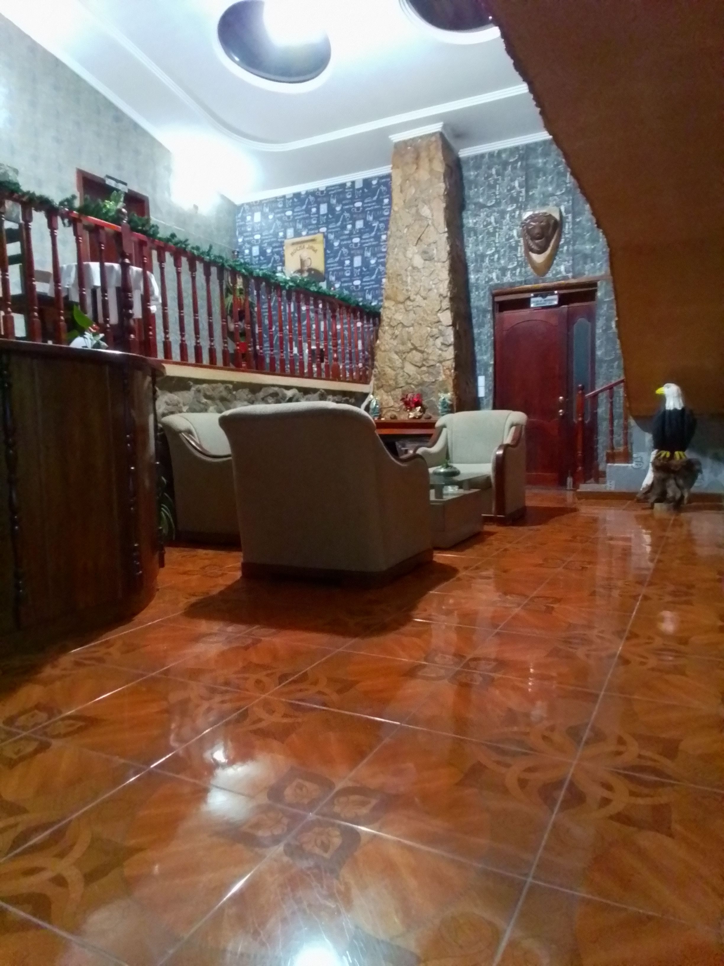 A spacious lobby with a high ceiling, a stone pillar, a wooden reception desk, and a staircase leading to an upper level.