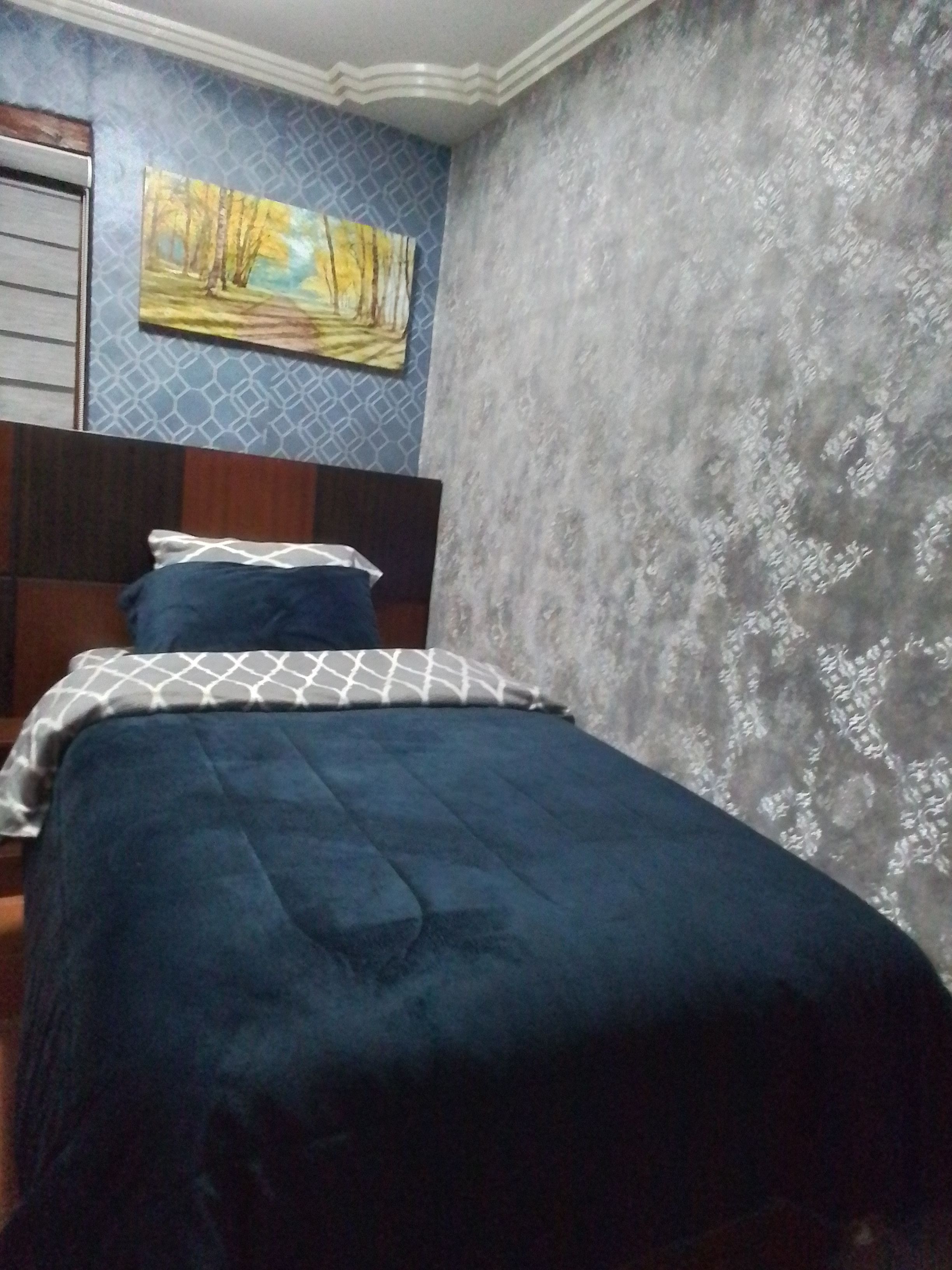 A bedroom with a bed, a painting on the wall, and patterned wallpaper.