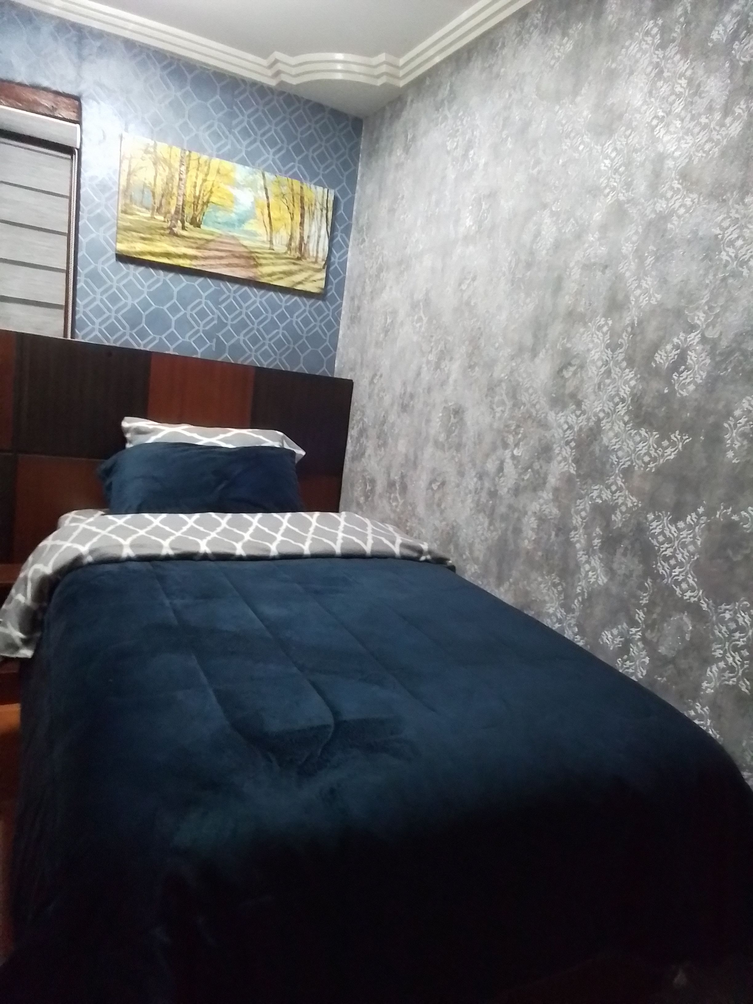 A bedroom with a bed, a headboard, a painting on the wall, and a patterned wallpaper.